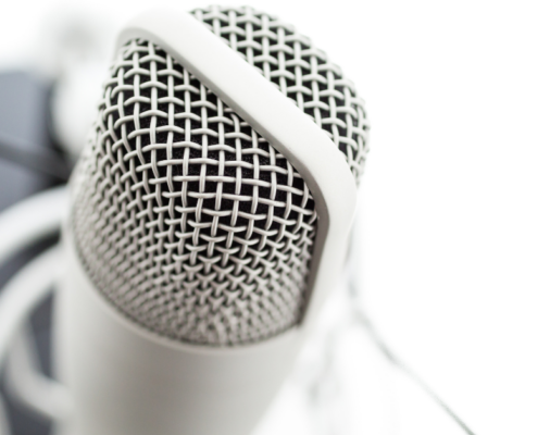 Nahaufnahme eines silbernen Mikrofons mit Gitter und weißer Stoßdämpferhalterung vor unscharfem Hintergrund. „MICRO AUDIO SYMPOSIUM“ und „Micro-Content“ werden in der unteren rechten Ecke angezeigt.