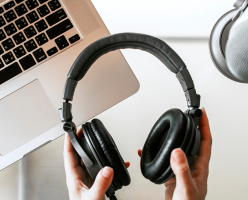 Eine Person hält schwarze Kopfhörer über einem Laptop, daneben ein Mikrofon – perfekt für die Aufnahme eines privaten Podcasts. Unten rechts erscheint der Schriftzug „Micro Audio Symposium“.