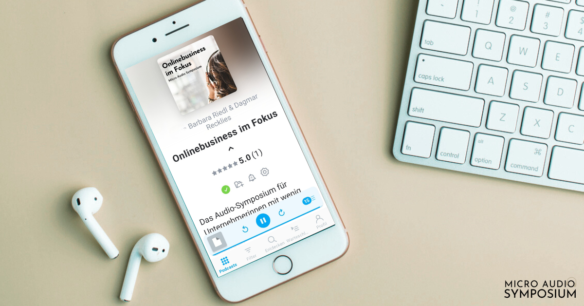 Ein Smartphone auf einer grünen Fläche zeigt das Hörbuch "Onlinebusiness im Fokus" an. In der Nähe befinden sich kabellose Ohrstöpsel, ein Teil einer kabellosen Tastatur und der Text "MICRO AUDIO SYMPOSIUM", der diesen Audio-Leitmagneten in Aktion zeigt.
