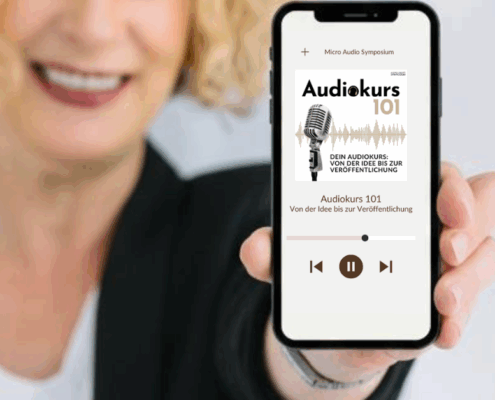 Eine lächelnde Person mit lockigem blondem Haar hält ein Smartphone in der Hand, auf dem ein Audiokurs mit dem Titel "Audiokurs 101" mit einem alten Mikrofon abgebildet ist - perfekt für alle, die neugierig auf Audiokurs vs. Podcast sind; die Wiedergabesteuerung ist auf dem Bildschirm zu sehen.