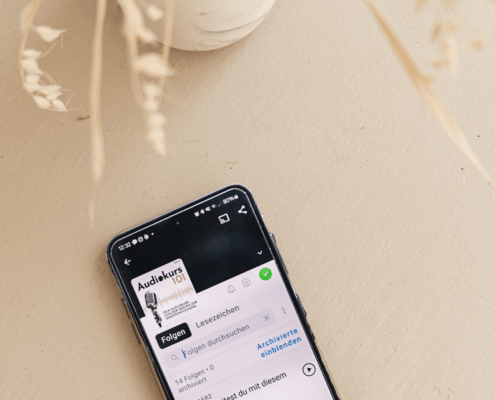 Ein Smartphone mit einer Podcast-App liegt auf einem hellen Tisch neben einer weißen Vase mit getrockneten beigen Pflanzen und spiegelt die Prinzipien des minimalistischen Designs wider. In der rechten unteren Ecke steht der Schriftzug "MICRO AUDIO SYMPOSIUM".