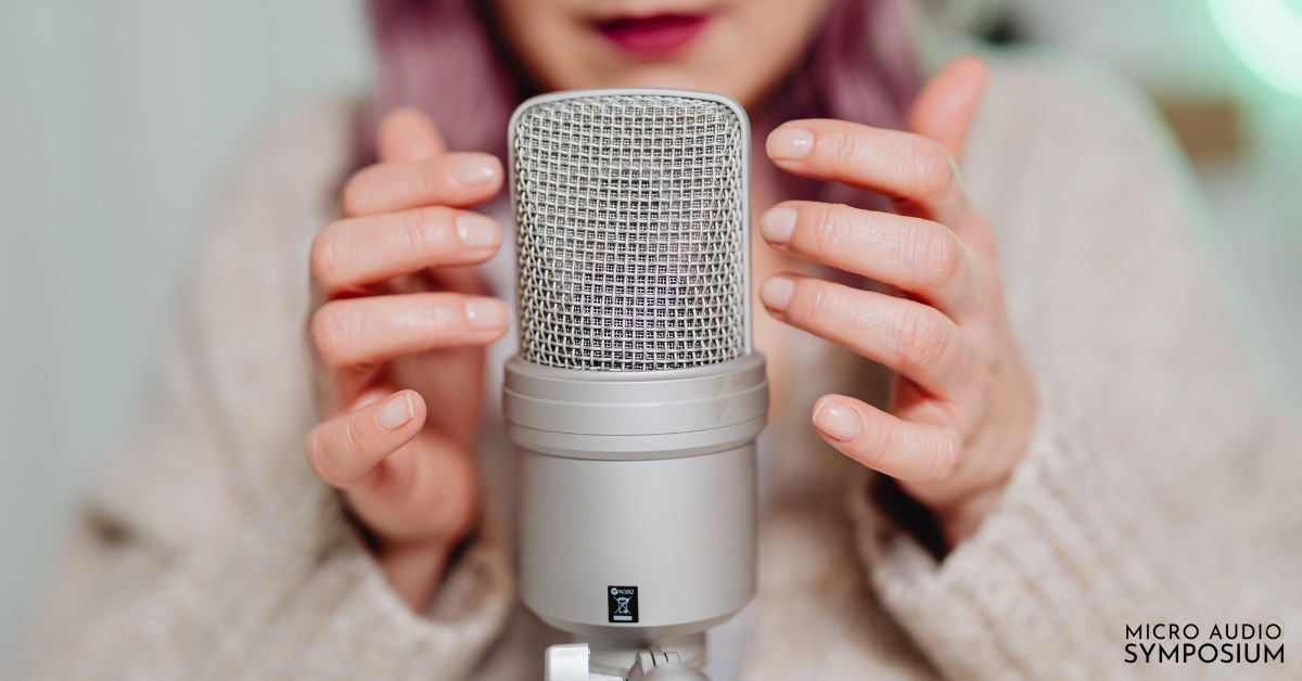 Eine Person mit hellrosa Nägeln hält sanft ein großes silbernes Kondensatormikrofon, das auf Podcasting 2025 hinweist, mit "MICRO AUDIO SYMPOSIUM" in der unteren rechten Ecke. Der sanft verschwommene Hintergrund verleiht dem Bild einen modernen Touch.