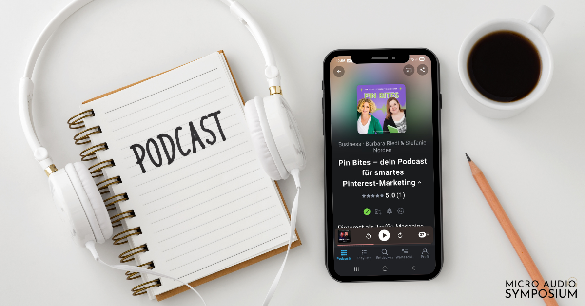 Ein Smartphone, das eine Podcast-Episode mit einem leuchtenden Podcast-Cover anzeigt, liegt auf einem weißen Schreibtisch neben einem Spiralnotizbuch mit der Aufschrift "PODCAST" und weißen Kopfhörern. In der Ecke ist das Logo des "Micro Audio Symposium" zu sehen.