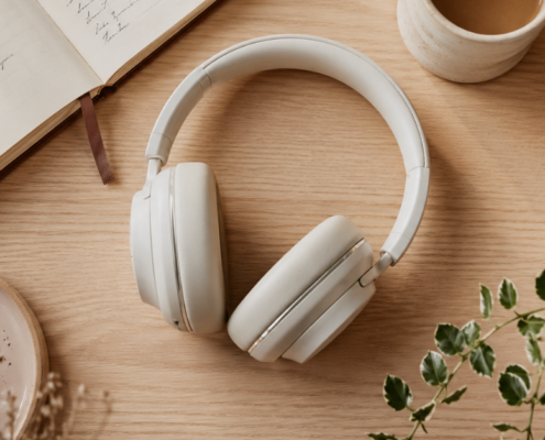Weiße Over-Ear-Kopfhörer auf einem Holztisch, umgeben von einem aufgeschlagenen Notizbuch mit Stift, einer Tasse Kaffee, einem Keramikteller und einer grünen Topfpflanze - die perfekte Kulisse für Ihre nächste Blogparade. In der Ecke erscheint "MICRO AUDIO SYMPOSIUM".