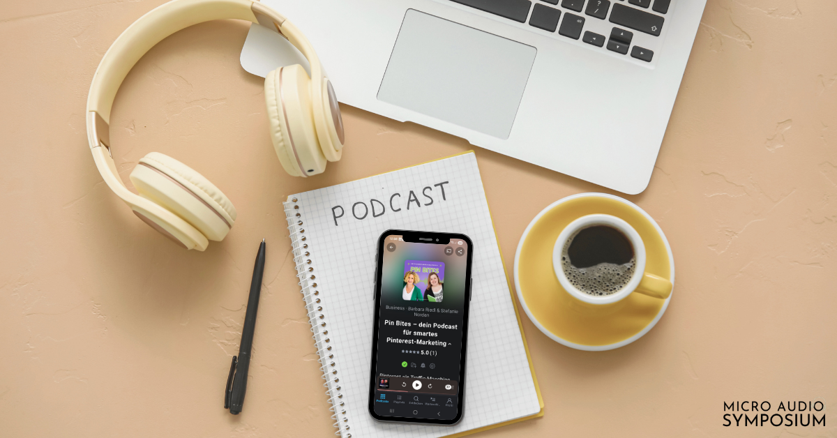 Auf einem beigen Schreibtisch liegt ein Smartphone, auf dem ein Podcast zu sehen ist, neben einem Notizblock mit der Aufschrift „PODCAST“, Kopfhörern, einer Tasse Kaffee und einem Laptop – die perfekte Grundausstattung für Ihre Podcast-Reise. In der rechten unteren Ecke steht „MICRO AUDIO SYMPOSIUM“.